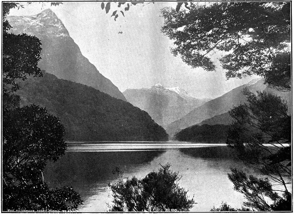 Photo of a lake. The foreground is surrounded by trees while in the background, there are snowy mountains being reflected by the lake.