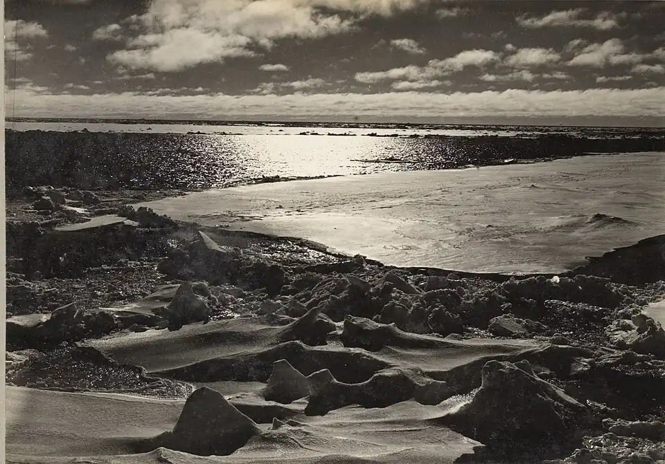 Photo of flat ice floes and open water with irregularly humped ice in the foreground