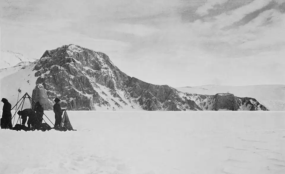 Landscape photo of a low rocky mountain with four men erecting a tent in the foreground