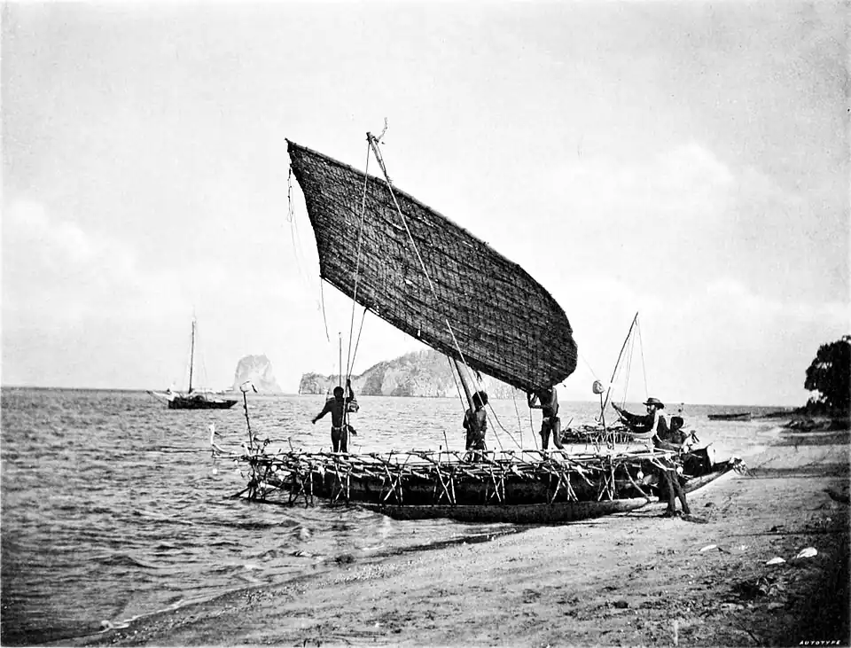 Black and white photograph of a sail boat moored on a beach with the sea in the background and islands on the horizon.