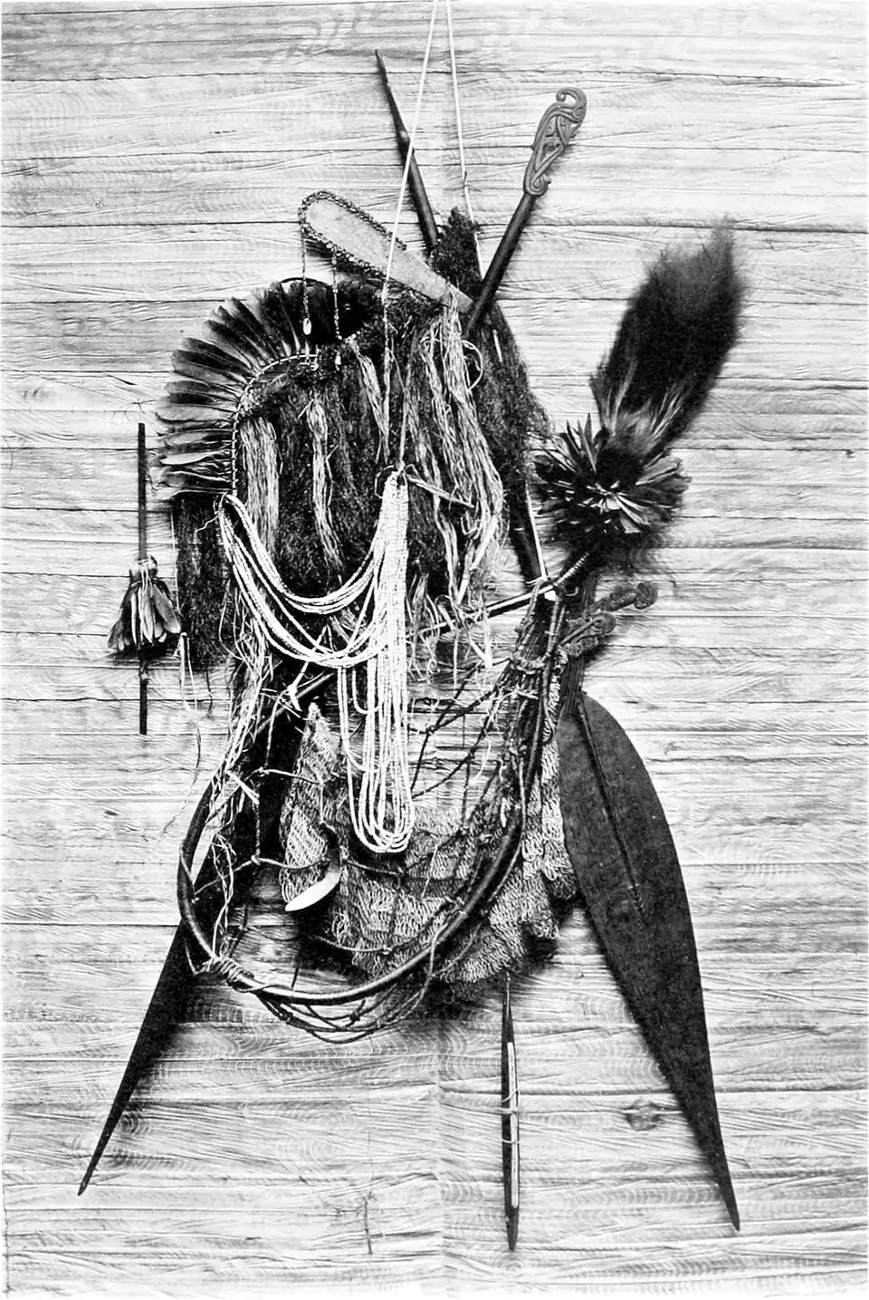 Black and white photograph of a collection of native implements, including paddles and ornaments.