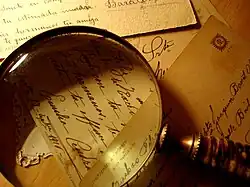 Photograph of a magnifying glass resting on a pile of mixed postcards.