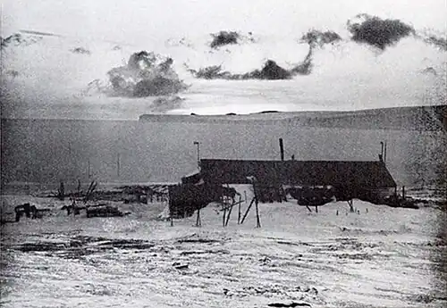 Photo of Scott's Hut and the bay beyond illuminated by occluded sunlight