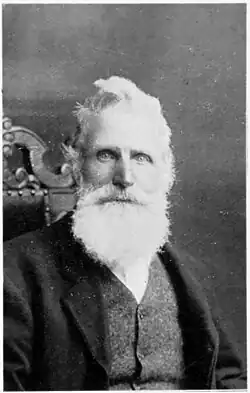 A portrait photo of Mr. James McDonald, now a sheep farmer from Dipton, Southland. He is sitting on an ornately backed chair, facing the front at a slight angle, with a full beard in a jacket and waist coat,
