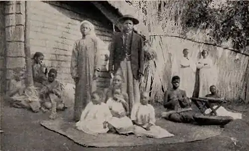 A man and woman standing in formal attire among a large group of children