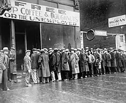 Unemployed men queued outside a Depression-era soup kitchen, opened in Chicago by Al Capone in February 1931. The storefront sign reads "Free Soup, Coffee and Doughnuts for the Unemployed."